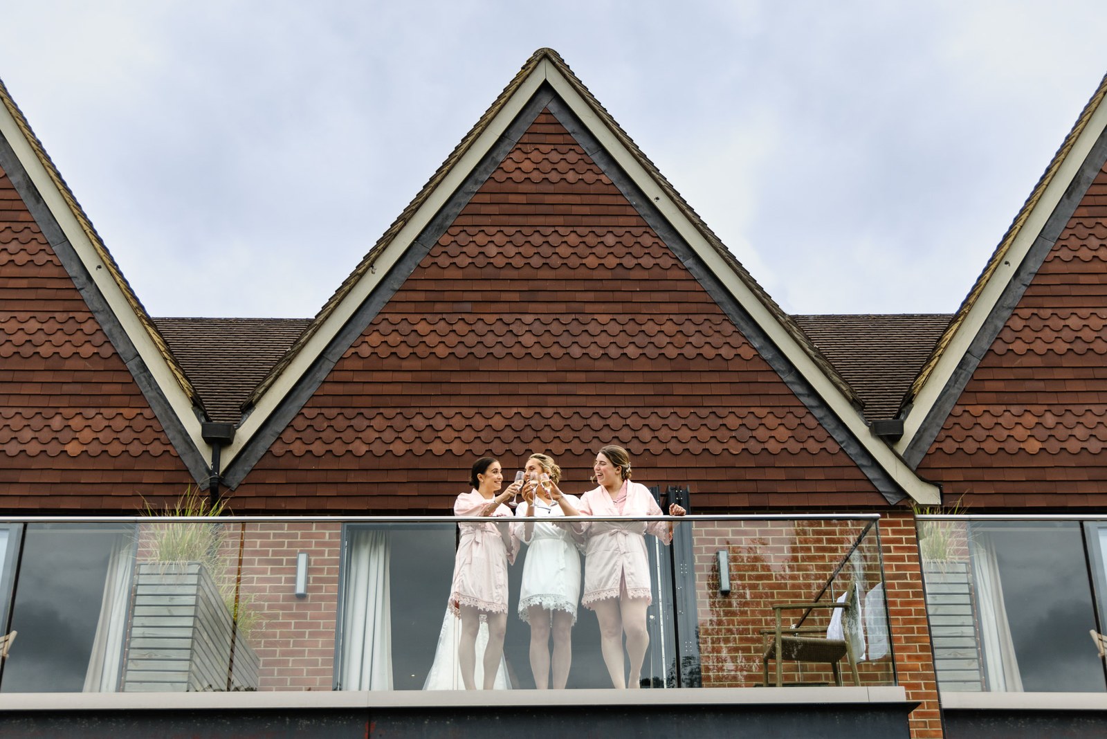 The bride and her bridesmaids on a balcony against the tiled gables of The Swan at Streatley