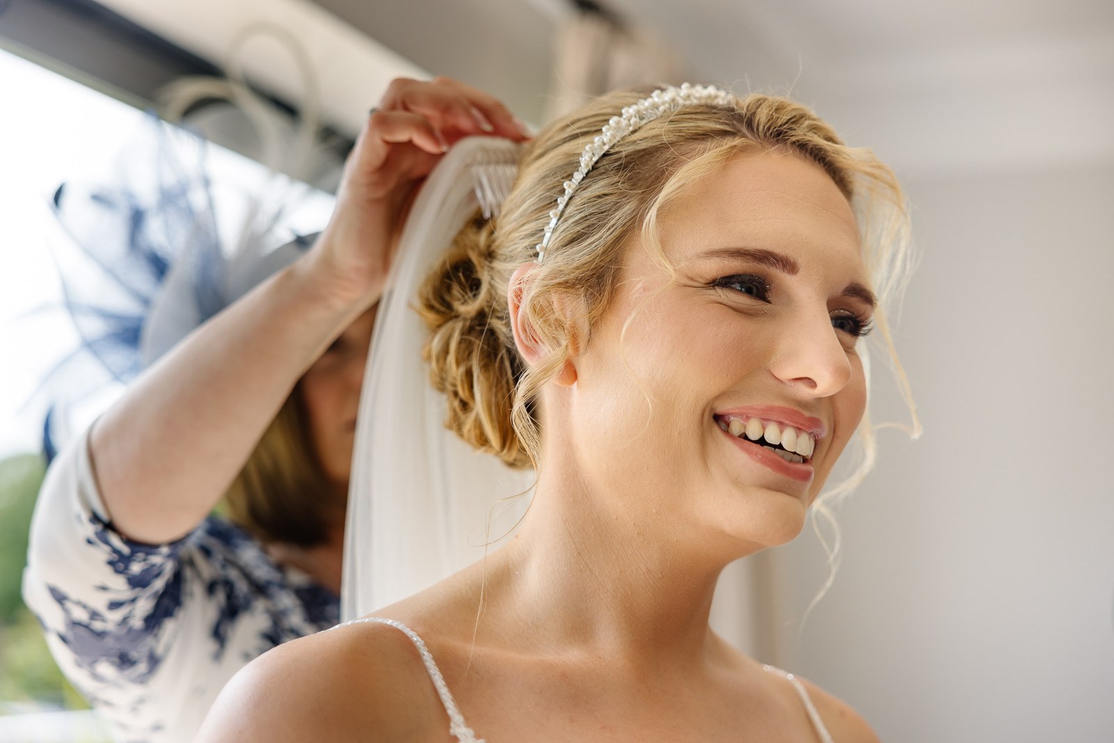 A helper securing the bride's veil as she smiles