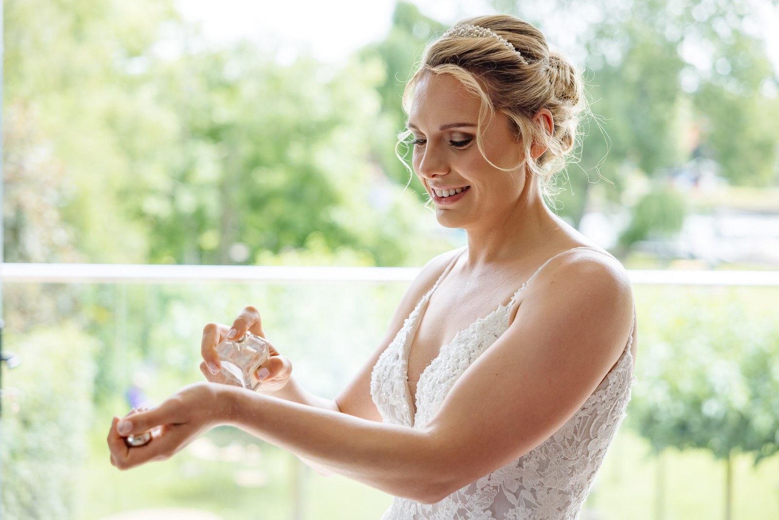 Bride in her gown spraying perfume by a bright window