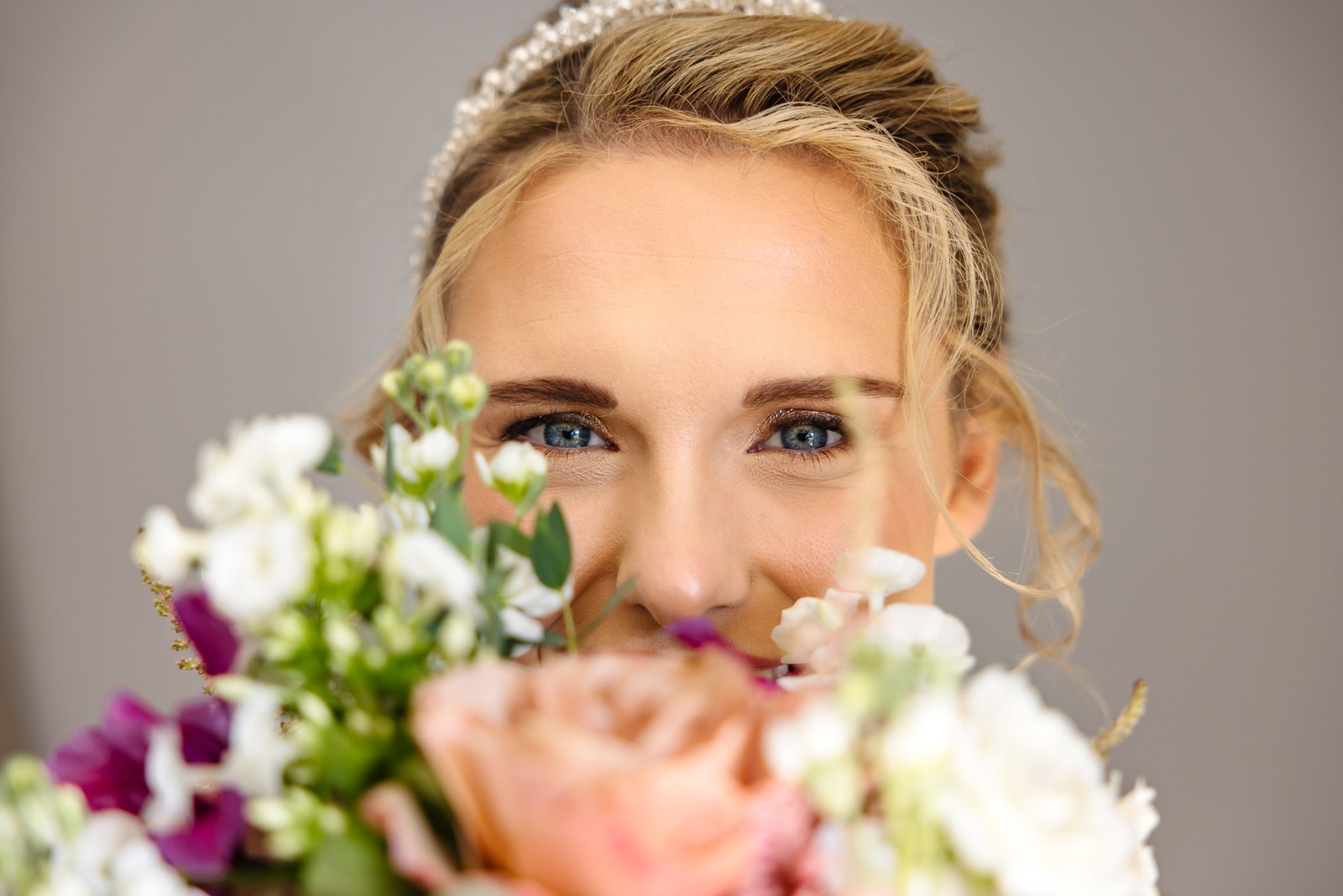 Bride peeking playfully over her bouquet of roses and sweet peas