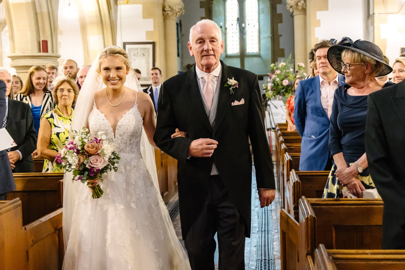 Bride walking down the church aisle on her father's arm as guests look on