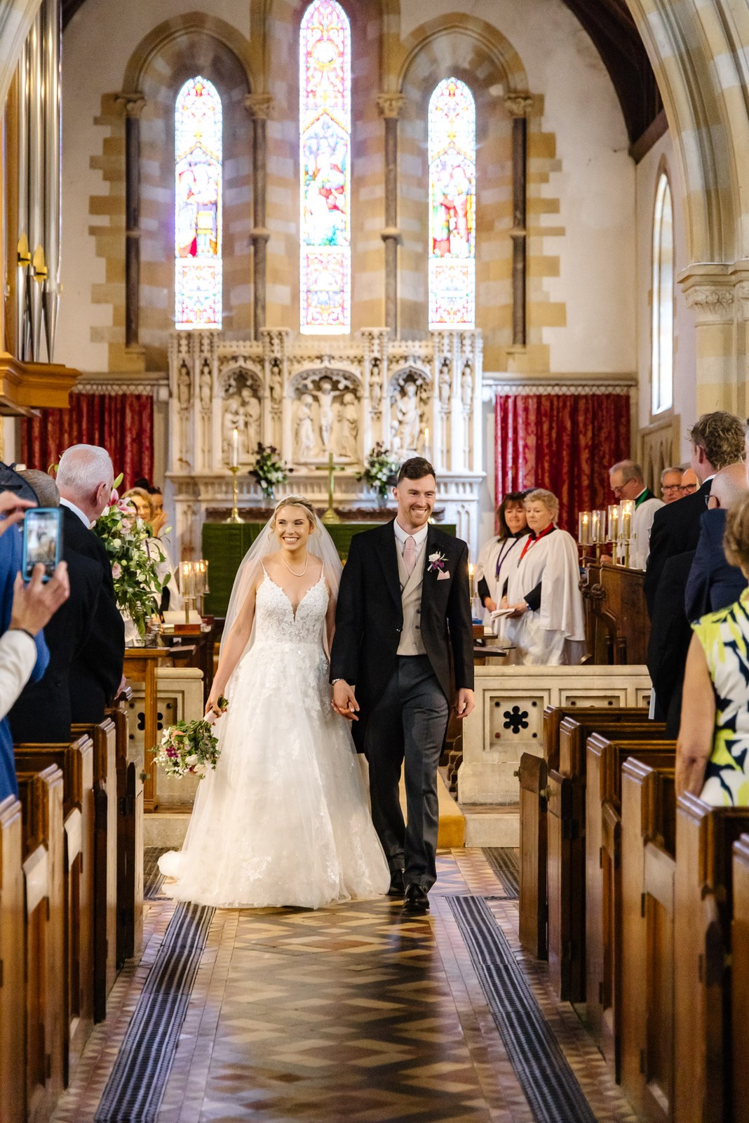 The newlyweds walking back down the aisle as guests photograph them