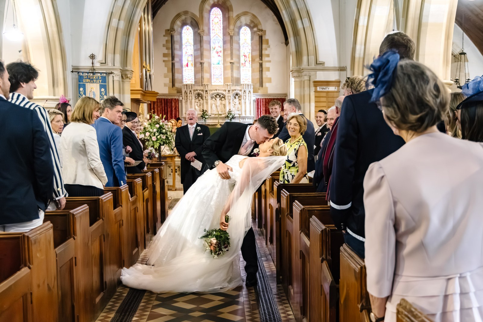 The couple sharing a kiss in the aisle as guests watch