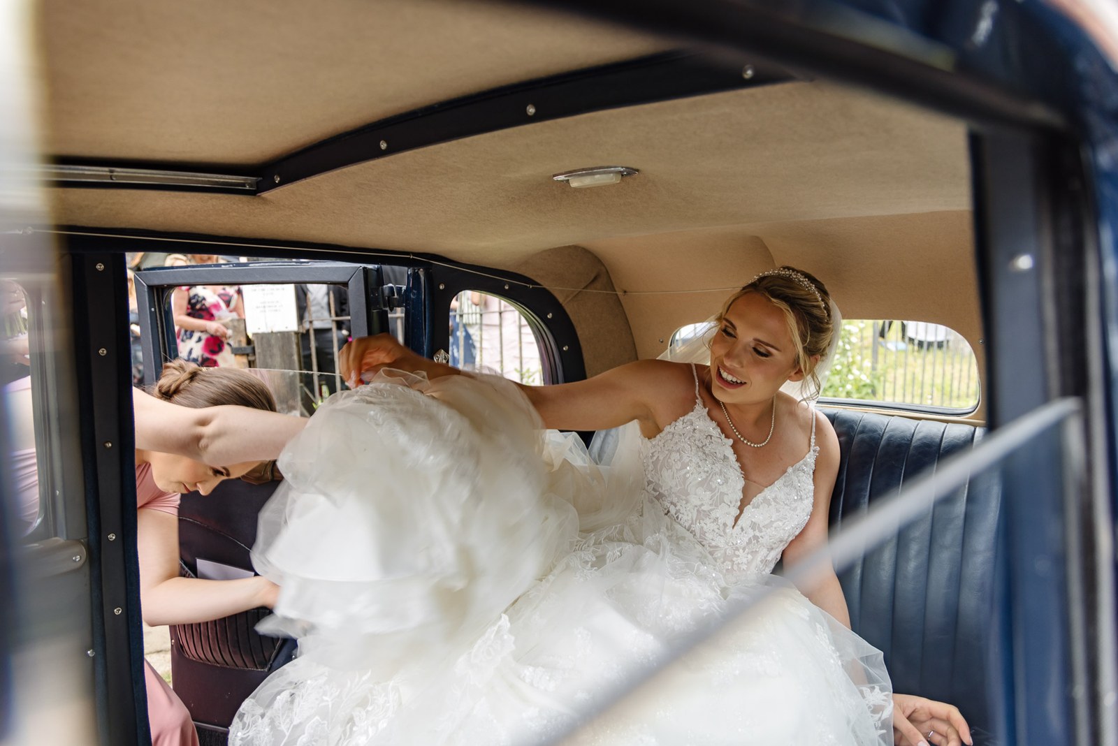 Bride gathering her gown as she climbs into the vintage wedding car