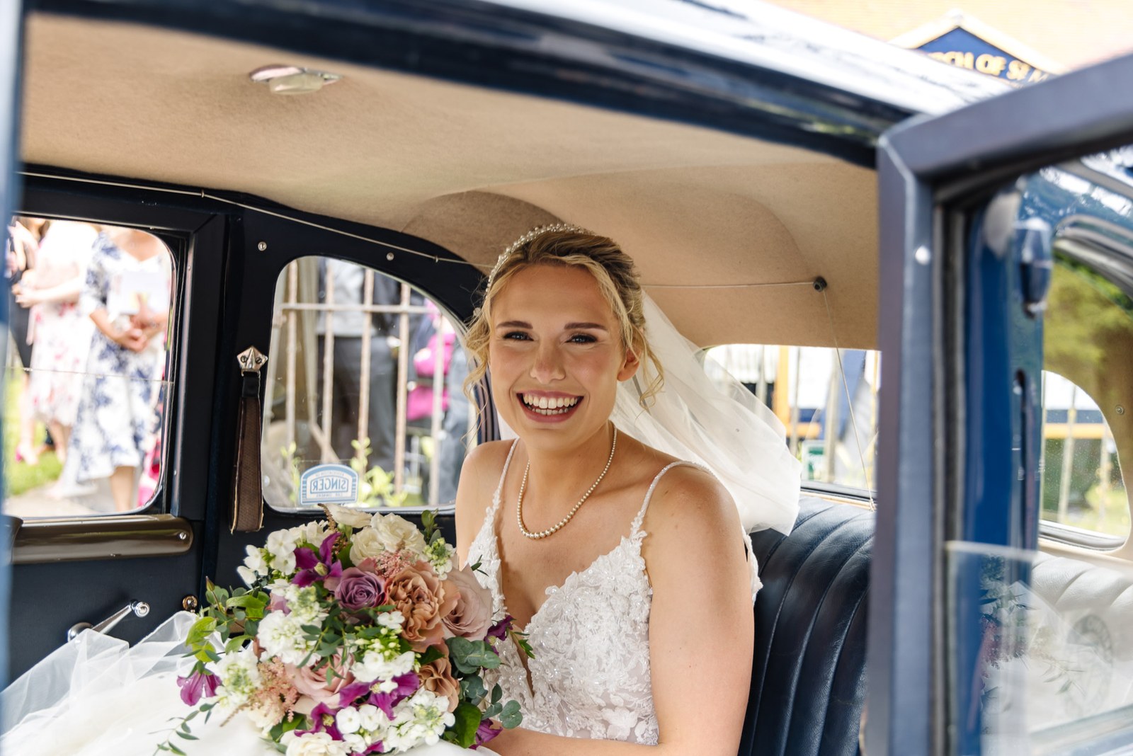 Bride seated in the wedding car holding her bouquet and smiling