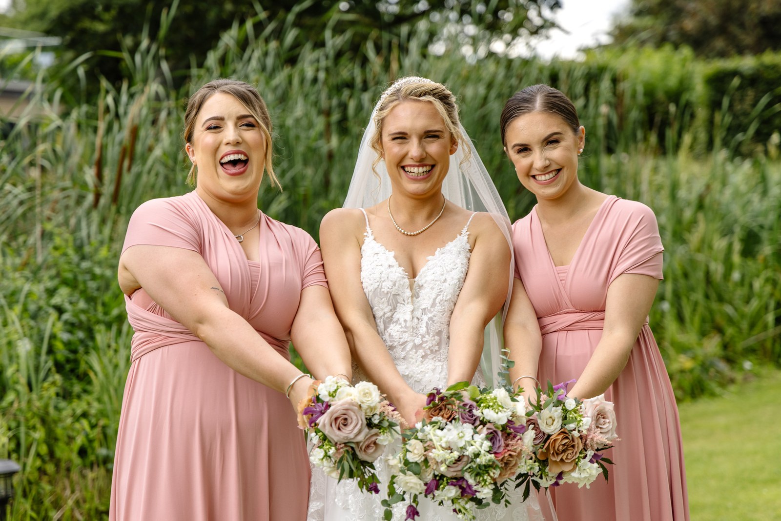 Bride laughing with her two bridesmaids in dusky pink by the reeds