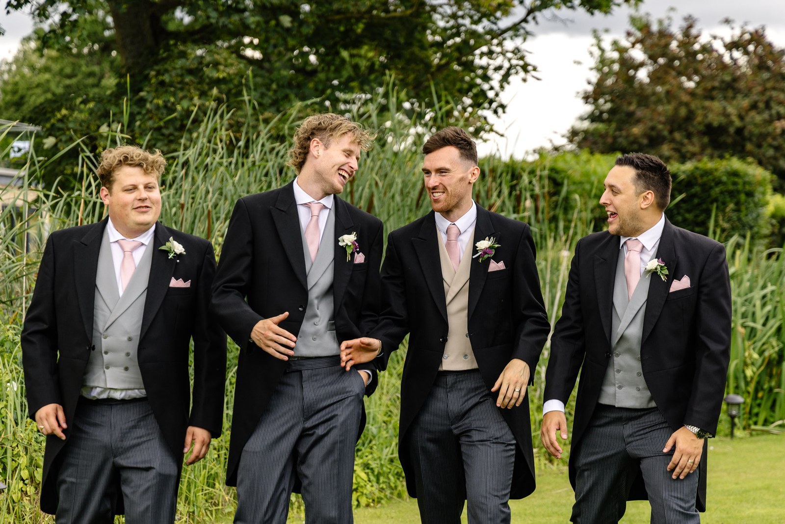 The groom strolling with his groomsmen beside the tall reeds