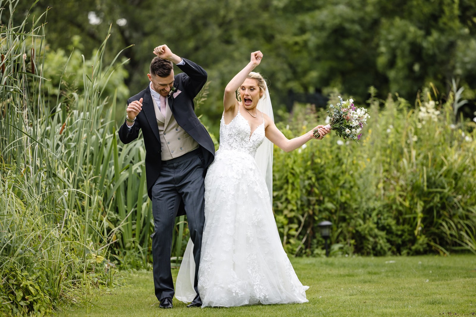 Bride and groom celebrating with arms raised on the lawn