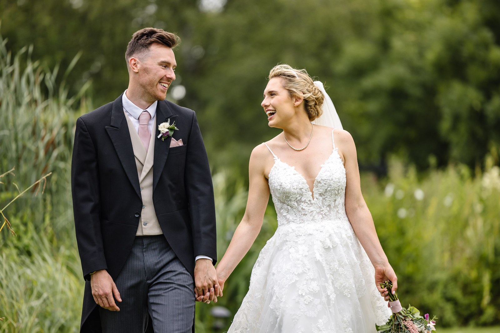 Bride and groom holding hands as they walk beside the reeds
