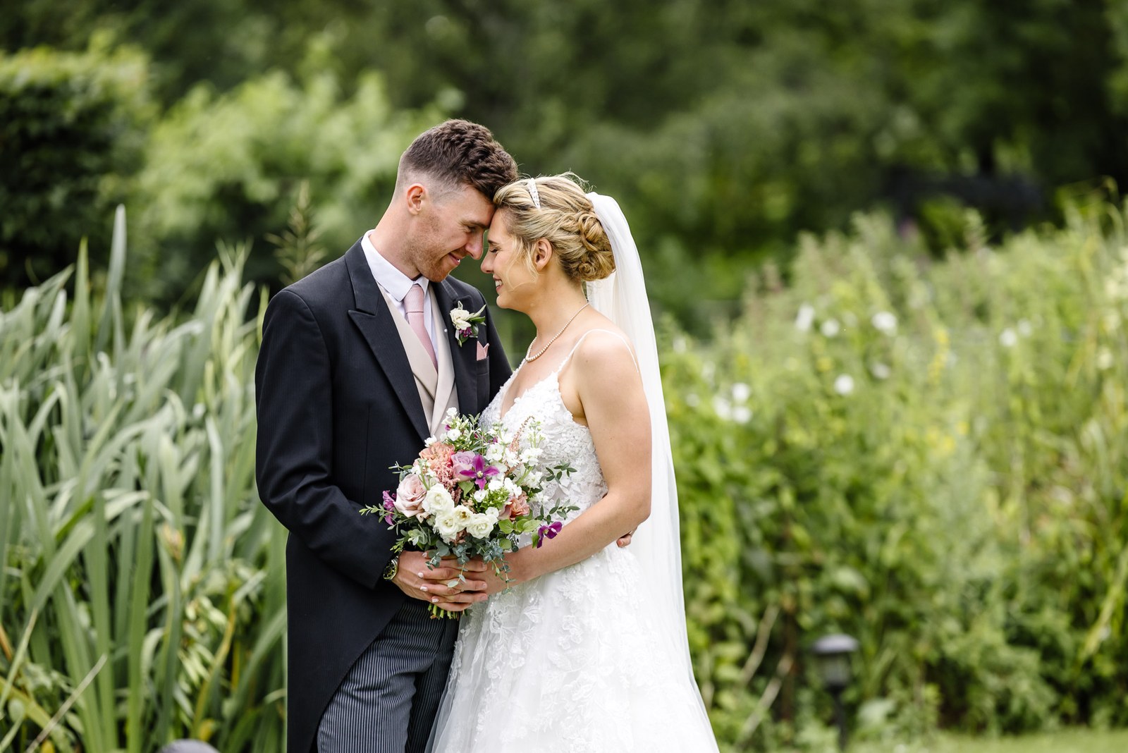 Bride and groom with foreheads together by the reeds, holding her bouquet