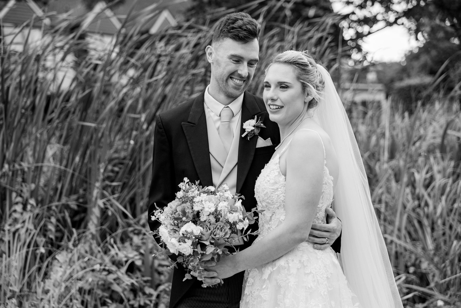 Black-and-white portrait of the couple embracing among the reeds