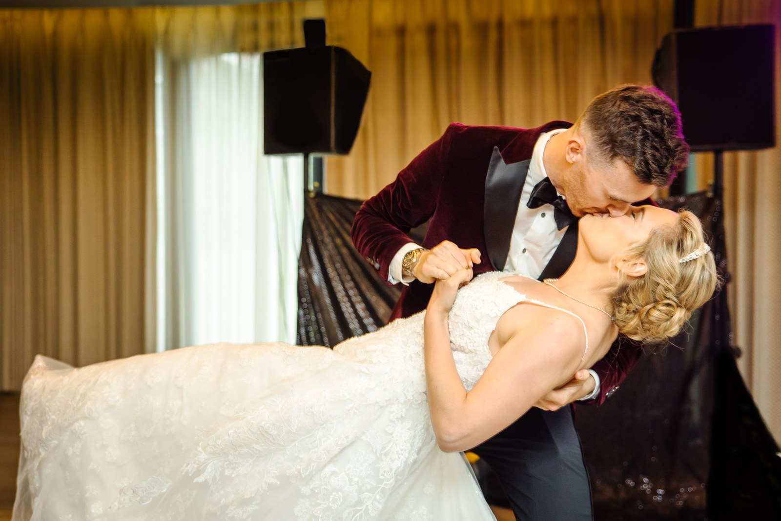 The groom in a velvet jacket dipping the bride into a kiss during their first dance