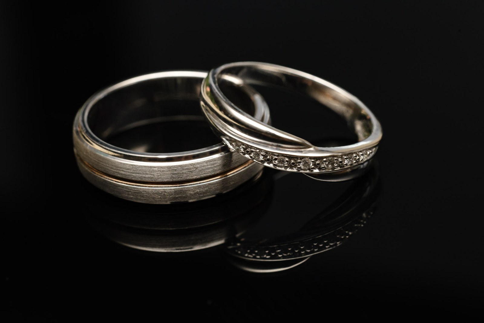 The two wedding rings on a dark reflective surface, one set with small diamonds