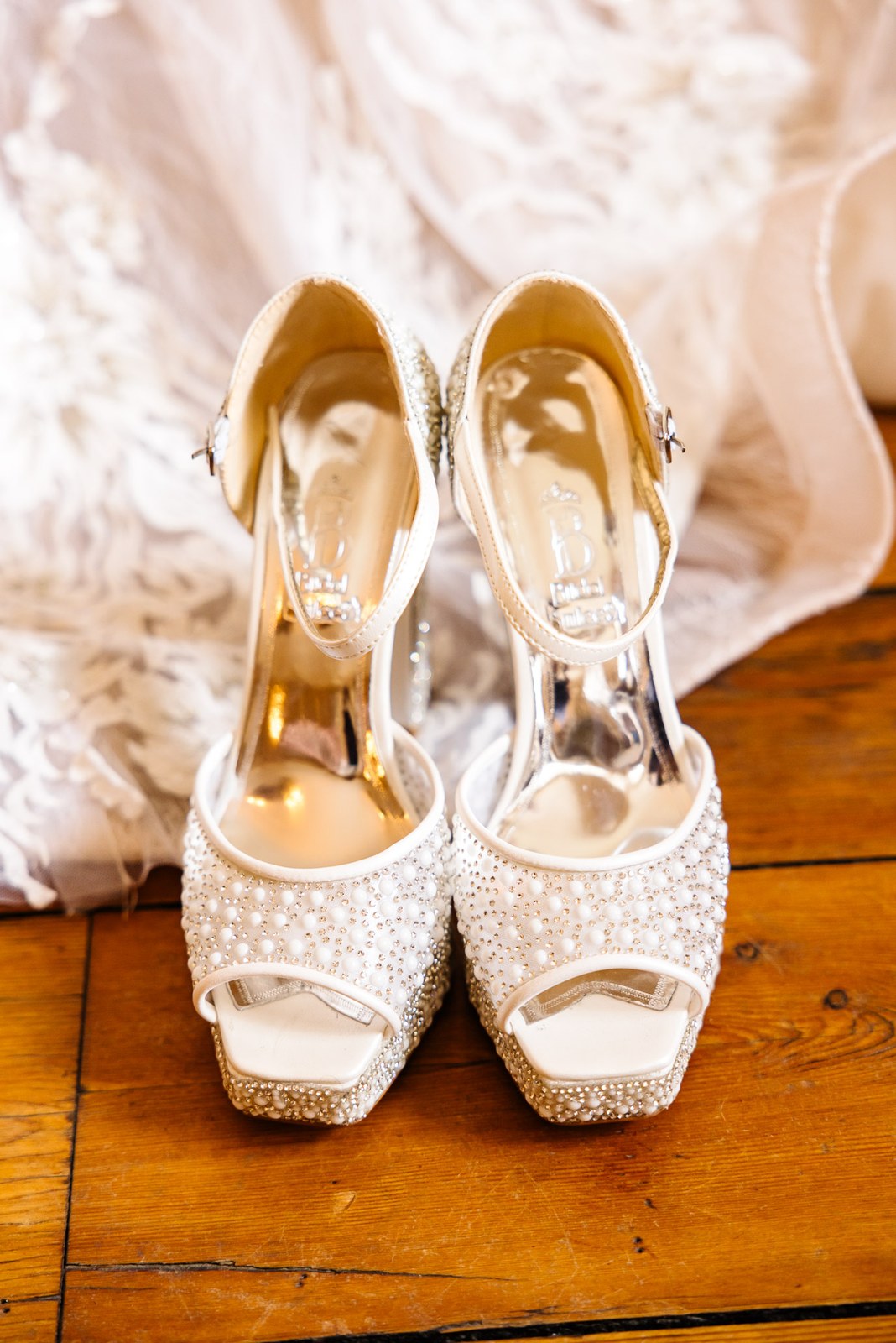 Pearl-embellished bridal heels resting on a wooden floor beside the gown