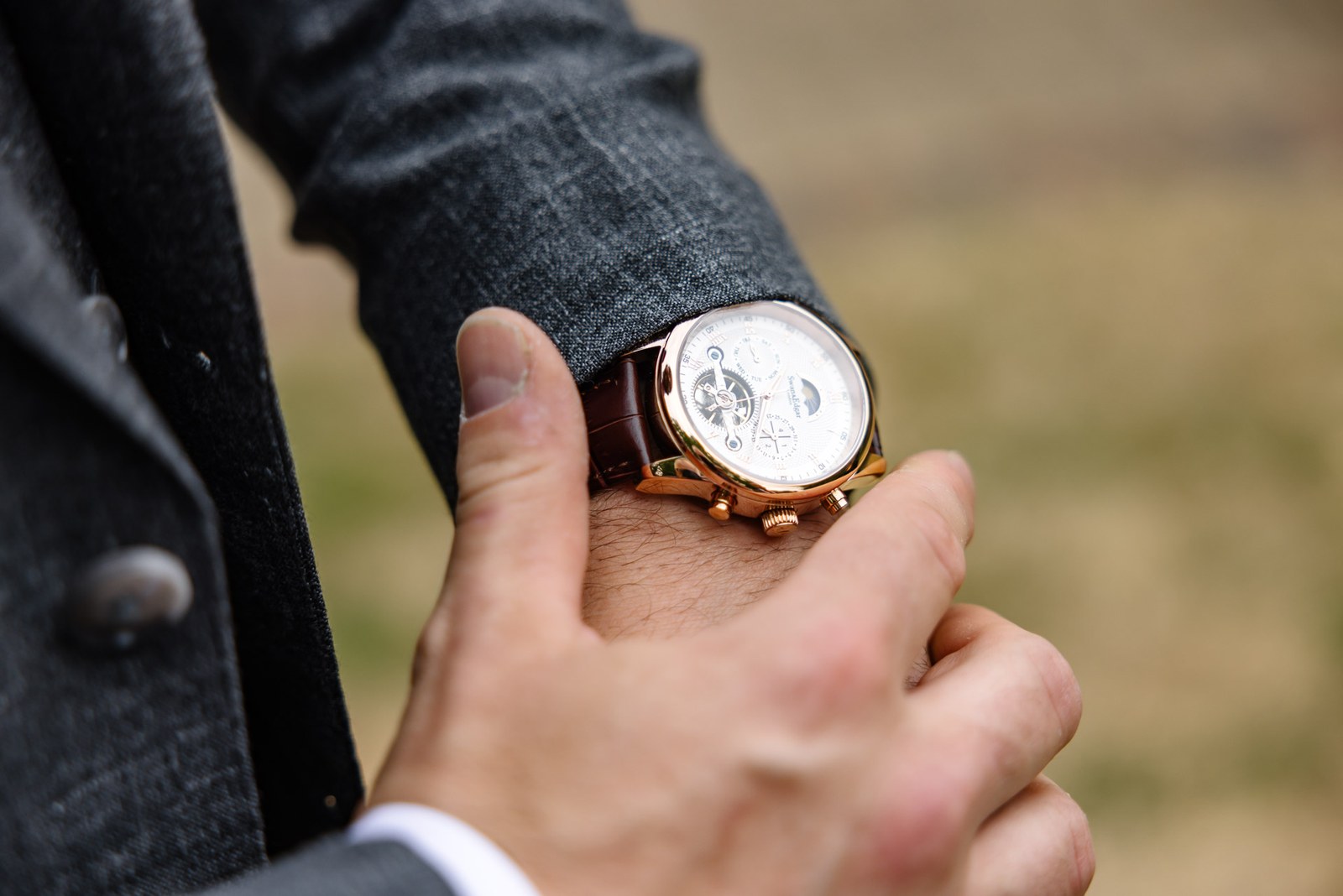 Close-up of the groom's ornate wristwatch on his grey suit sleeve