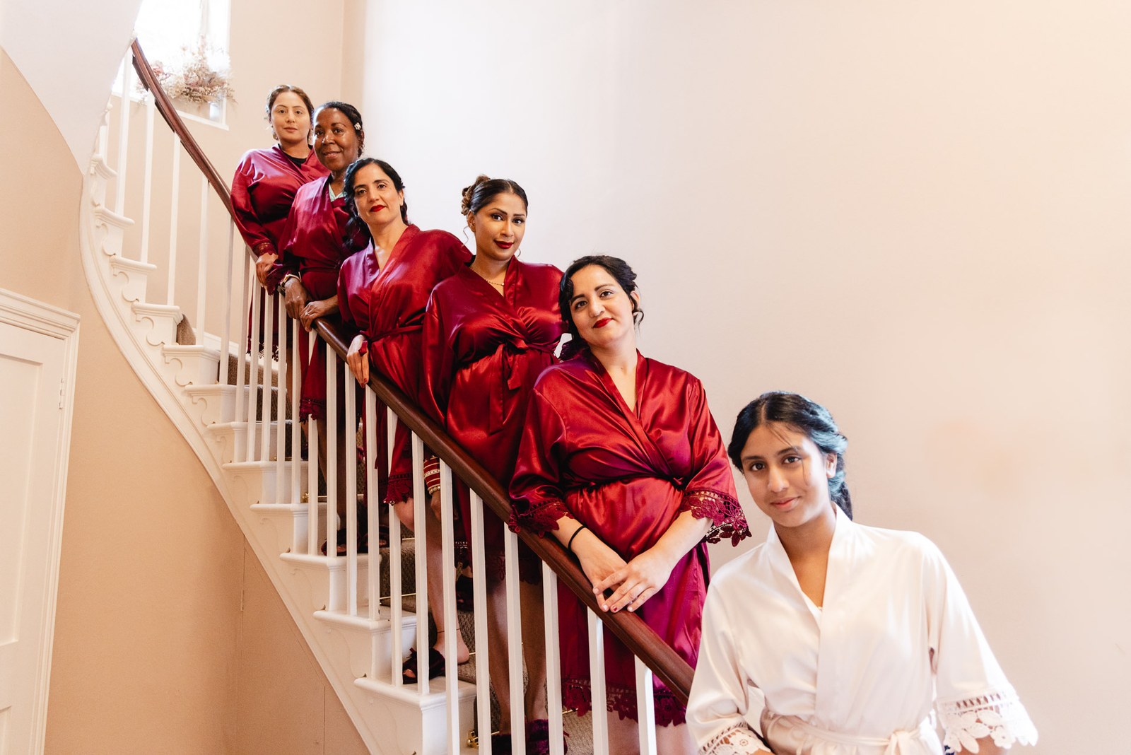 Bridesmaids in red satin robes posing along a curving white staircase