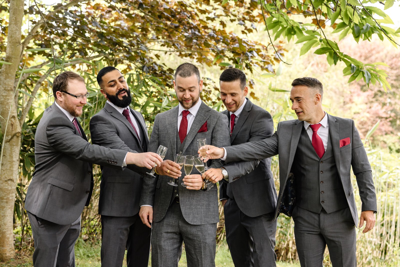 The groom and his groomsmen raise a champagne toast beneath the trees