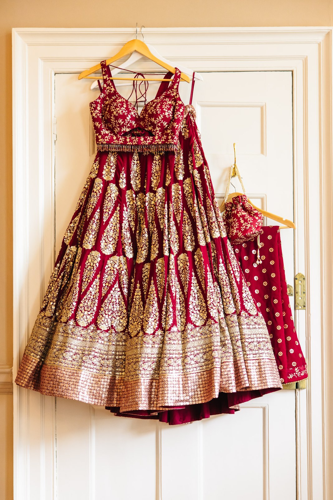 A red and gold embroidered bridal lehenga hanging on a panelled door