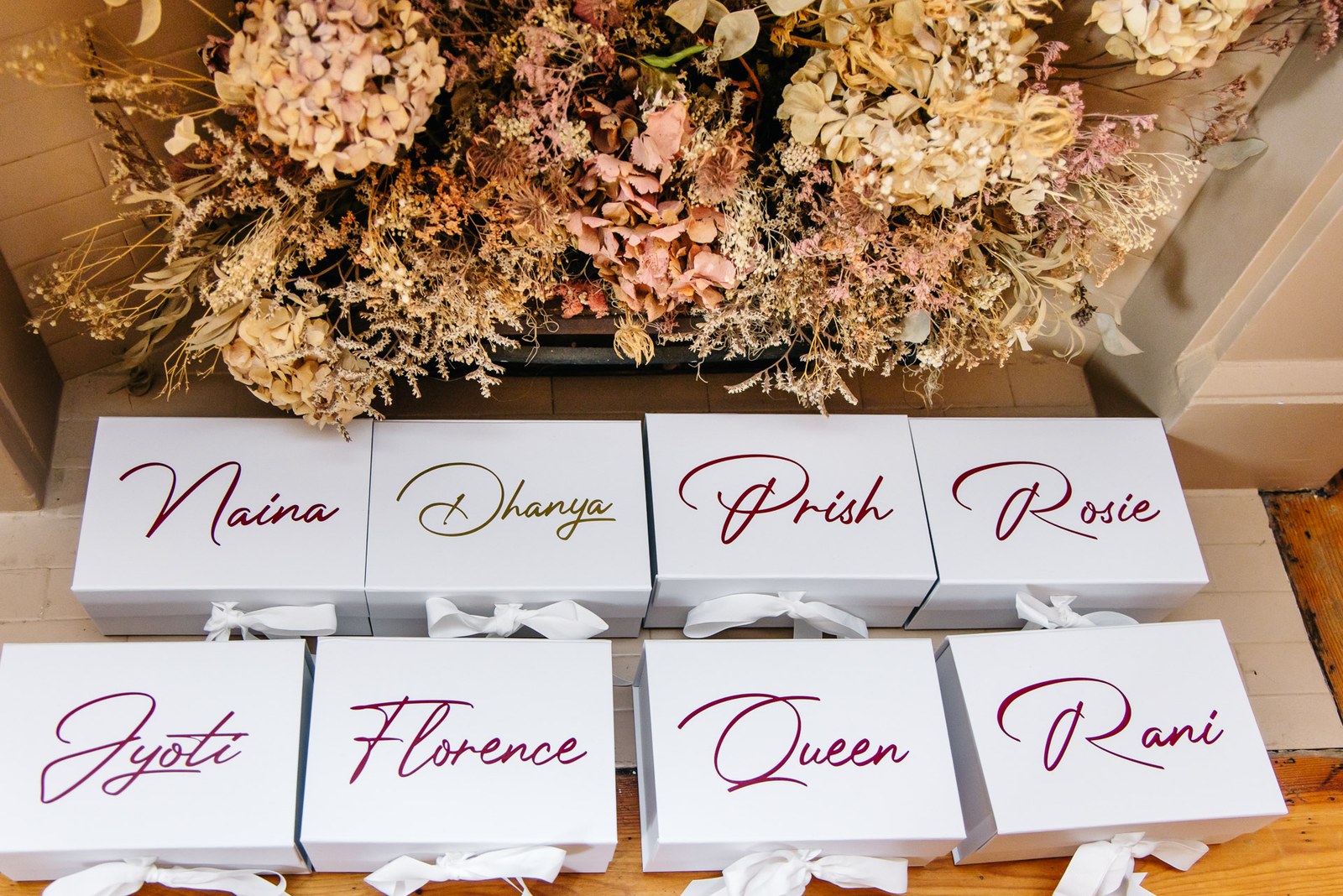 Personalised bridesmaid gift boxes named in script beneath a dried floral display