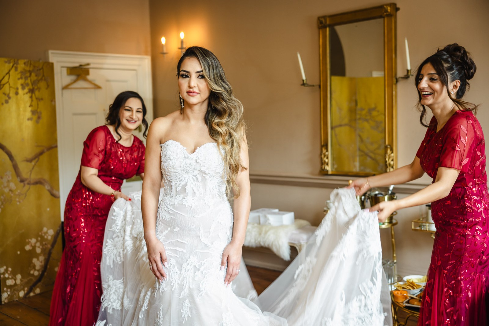 Attendants arranging the train of the bride's gown as she stands ready