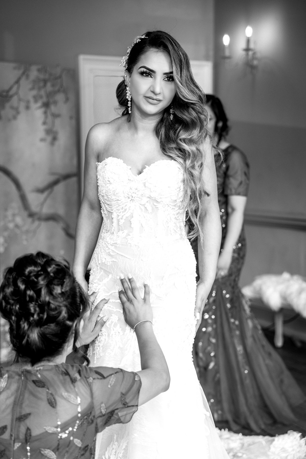 Black-and-white moment of an attendant smoothing the bride's gown
