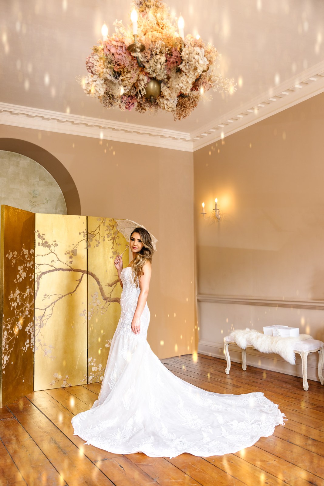 Full-length bride with a long train before the gold screen and floral chandelier