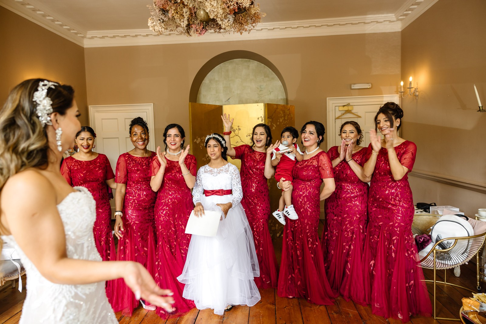 The bride with her red-gowned bridesmaids and flower girl in a bright room