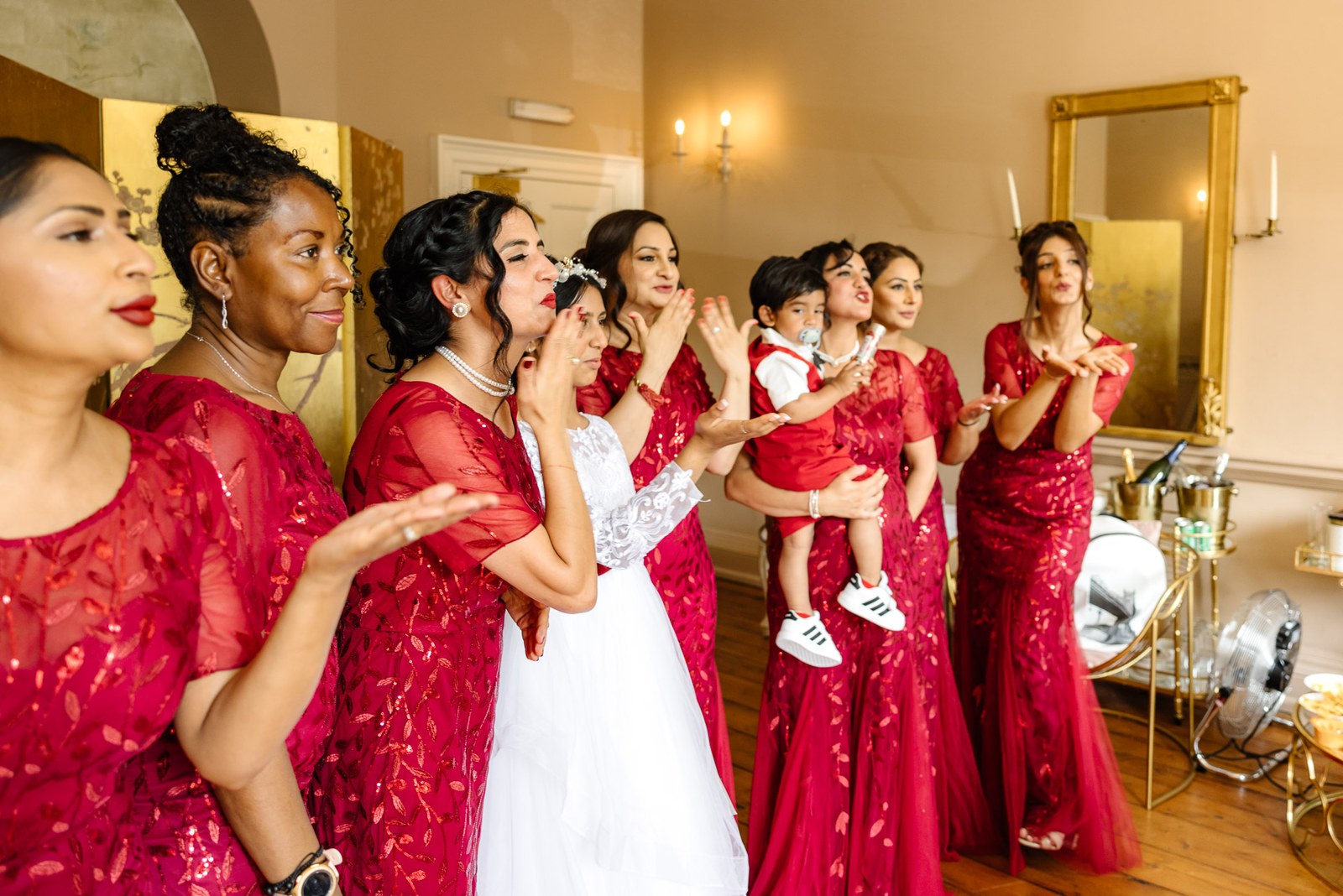 Bridesmaids in red admiring the bride, one holding a small child