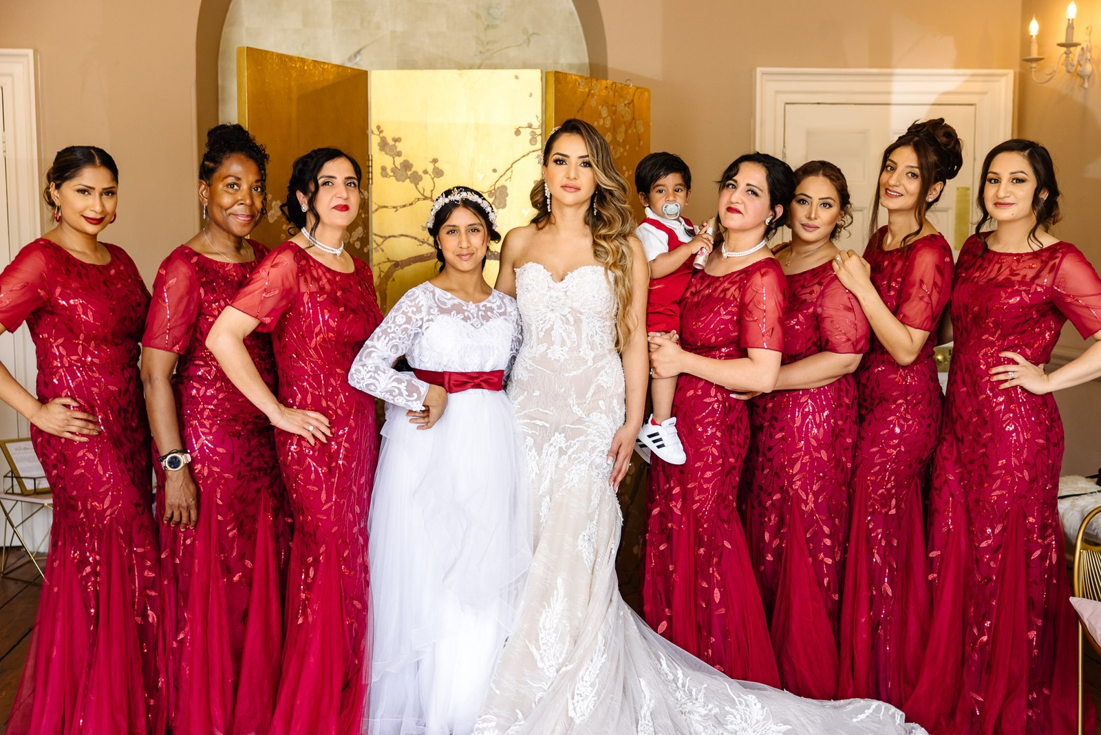 The bride and flower girl framed by bridesmaids before the gold screen