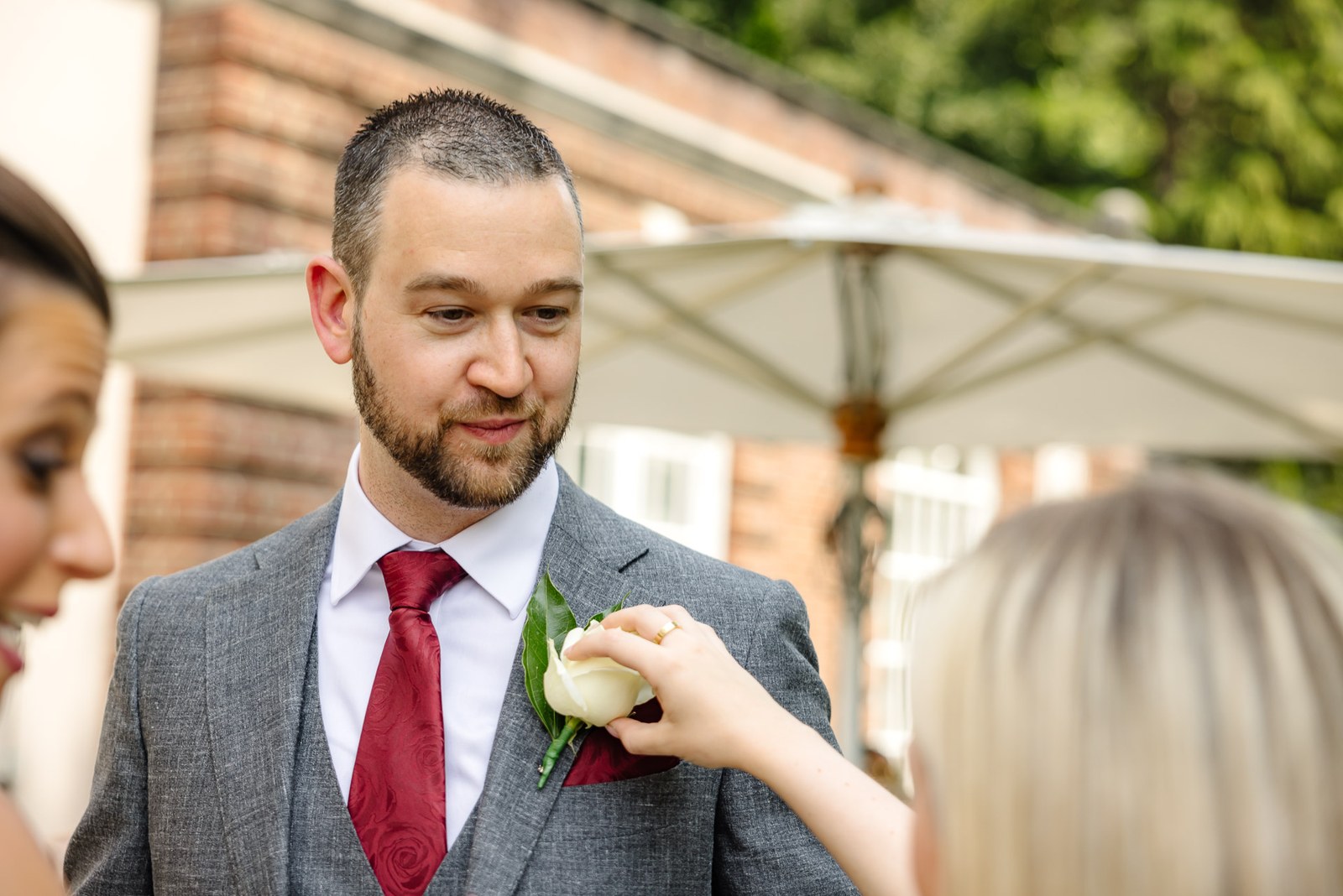A guest hands the groom his white rose buttonhole in the garden