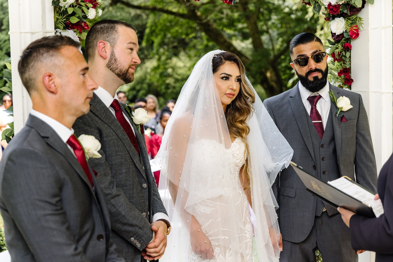 Bride and groom beneath the floral ceremony arch as the celebrant speaks