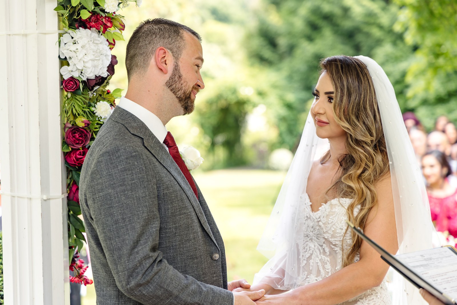 The couple hold hands facing each other under the flower-decked ceremony arch