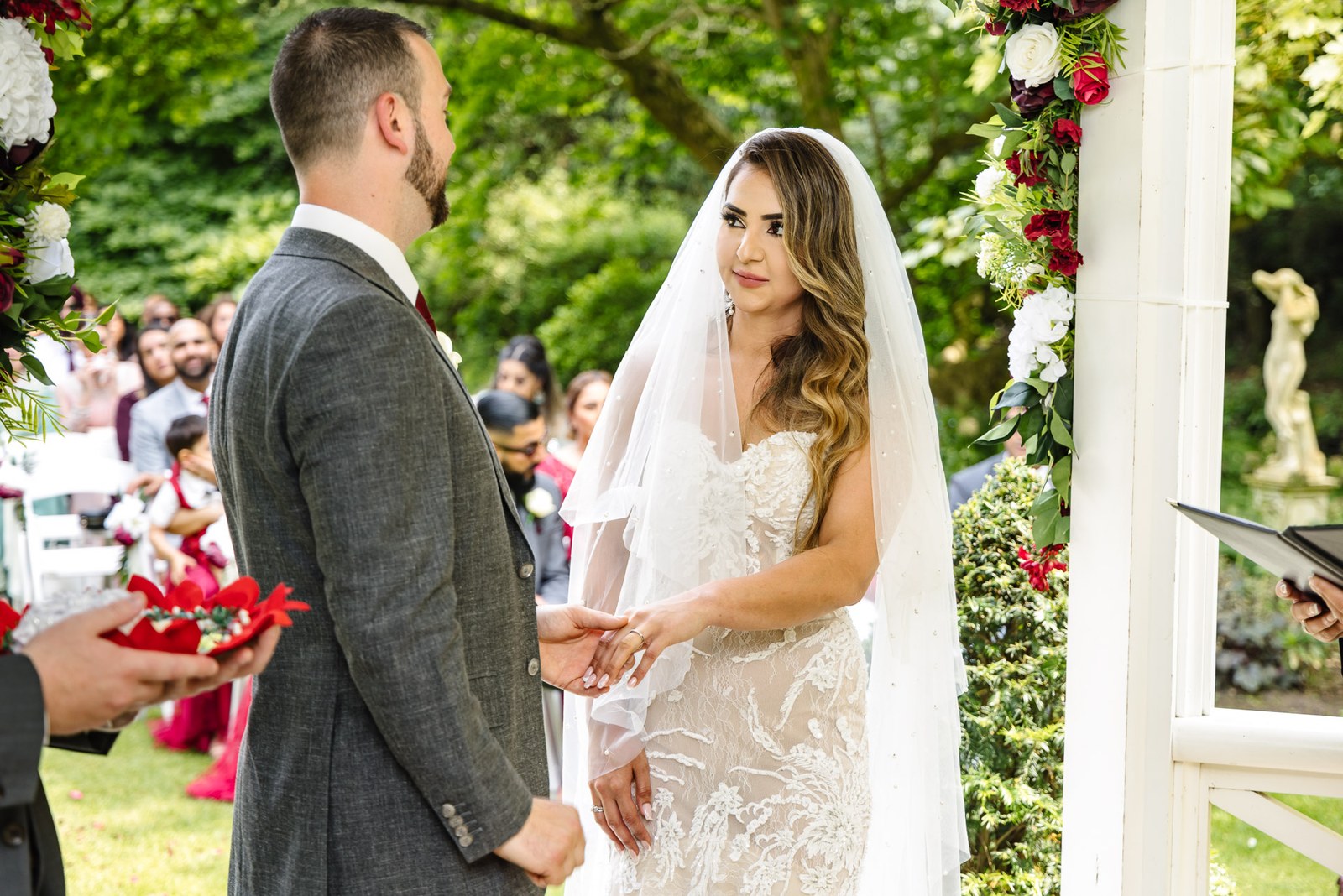 Bride and groom clasp hands during the outdoor ceremony, guests behind