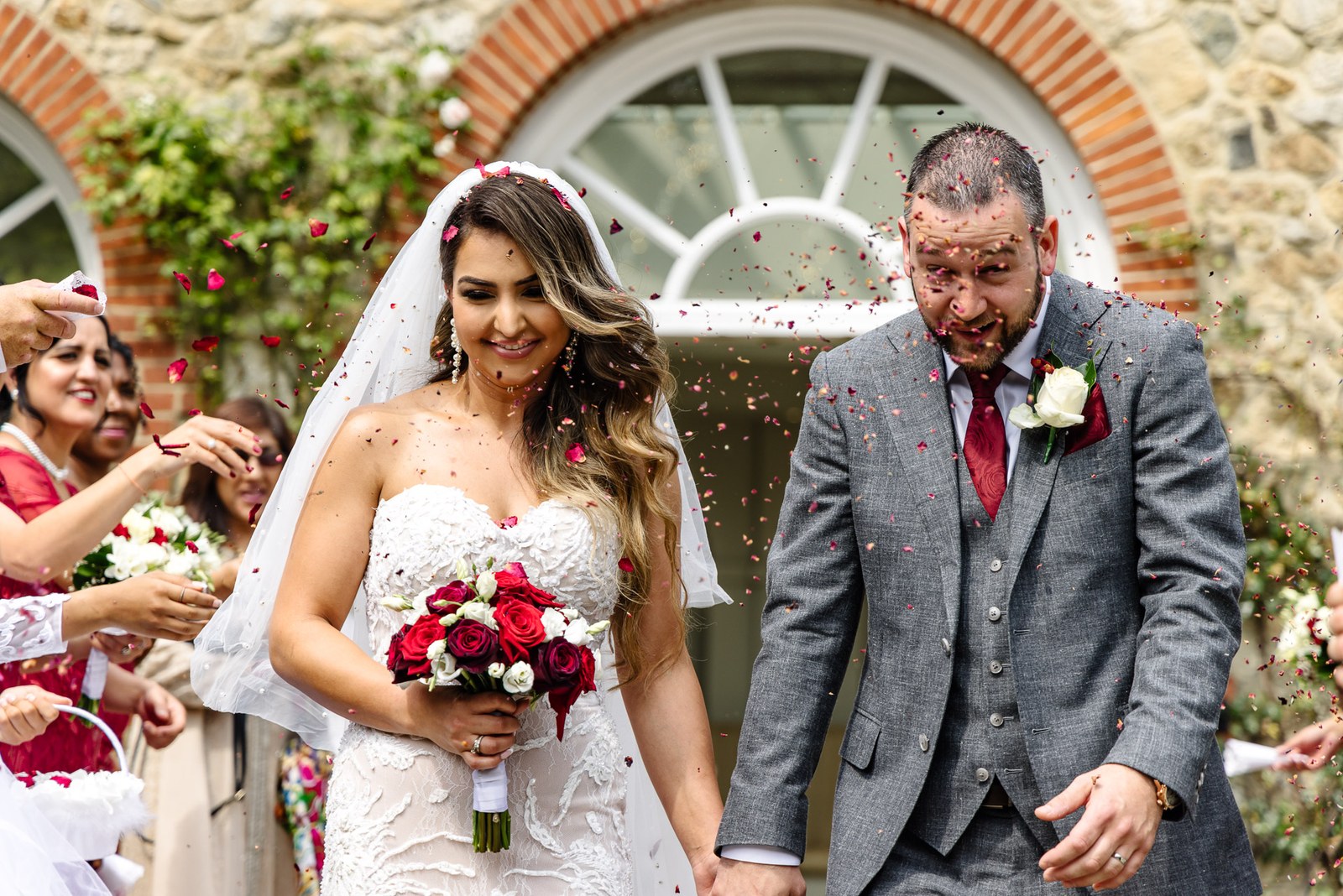 Confetti rains over the couple by a brick archway at The Orangery, Maidstone