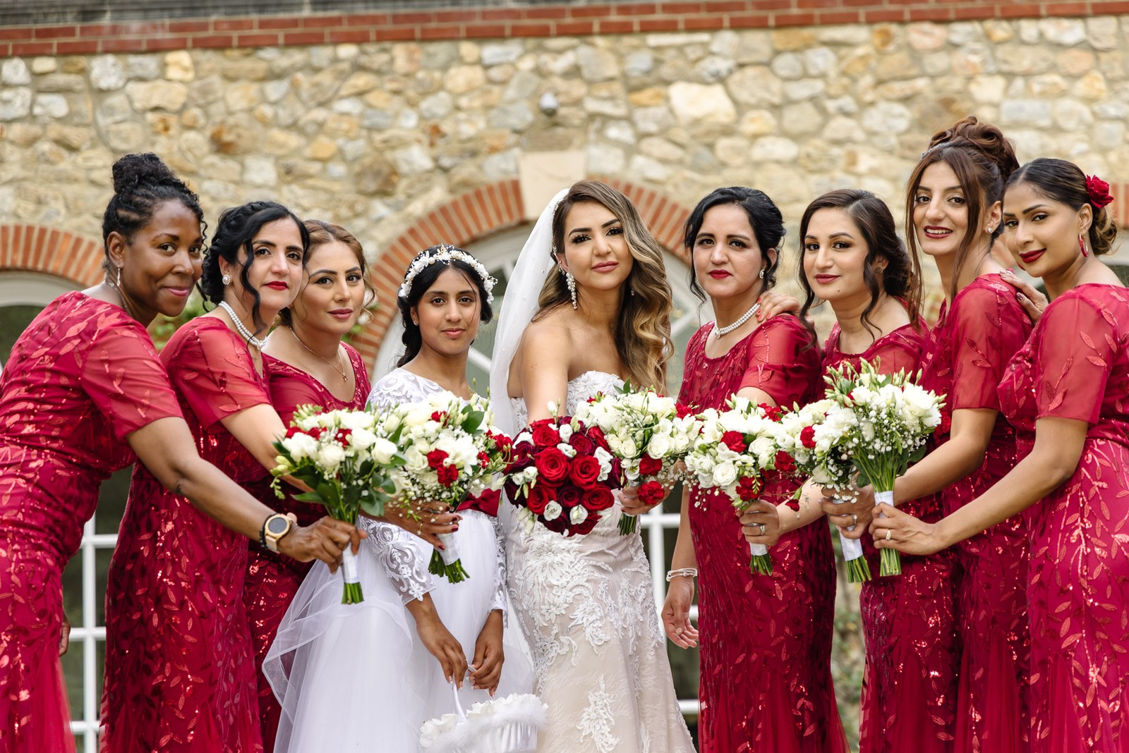 Bride and bridesmaids lean in together with their bouquets by the brick arches