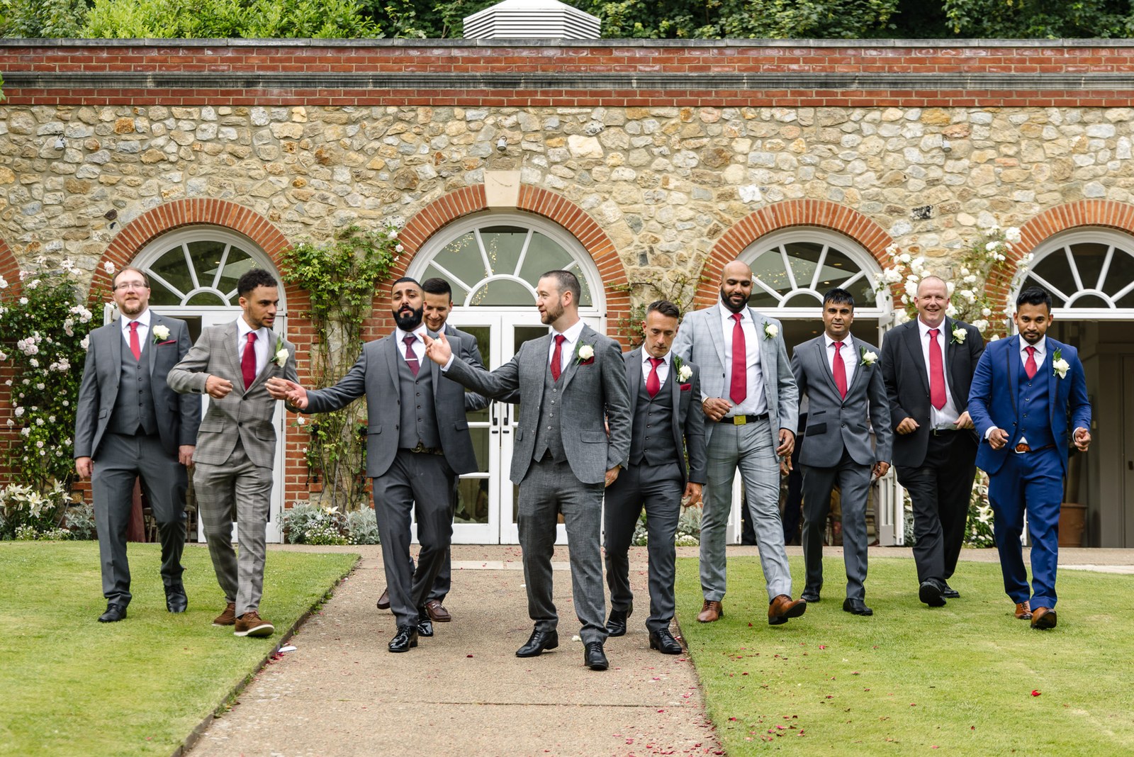 The groom and his groomsmen stroll before the arched frontage of The Orangery