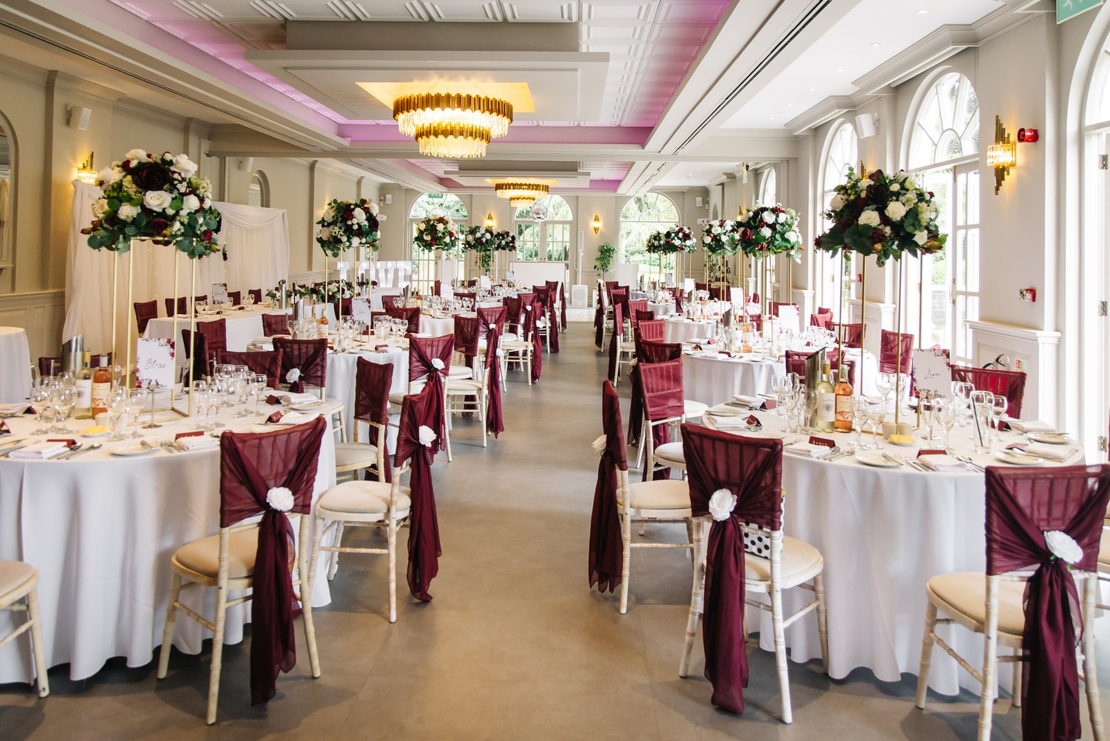 The Orangery dining room set with round tables, burgundy sashes and tall floral centrepieces