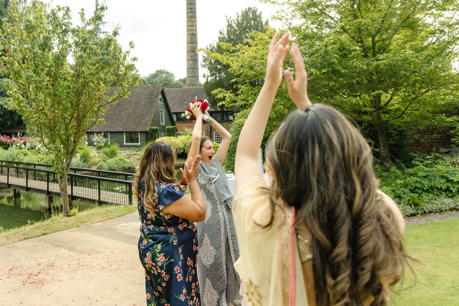 Guests cheer as one holds the caught bouquet aloft in the gardens