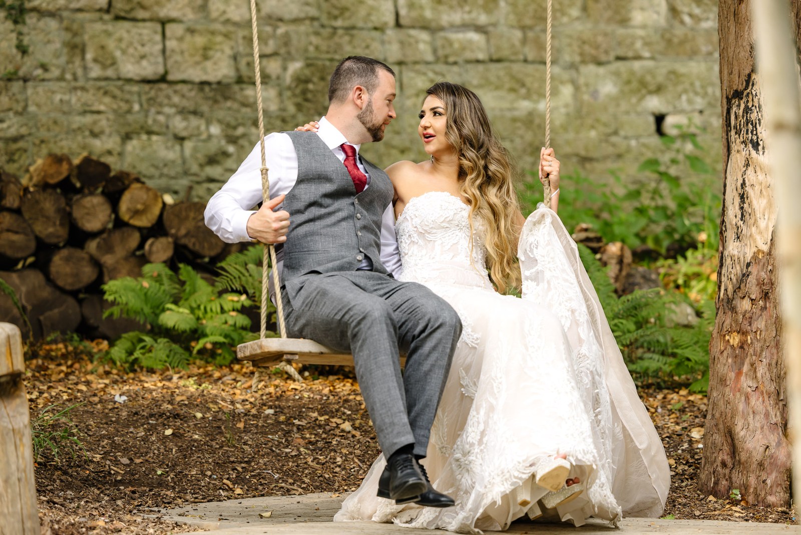 Bride and groom perched on a rustic rope swing beside a log store