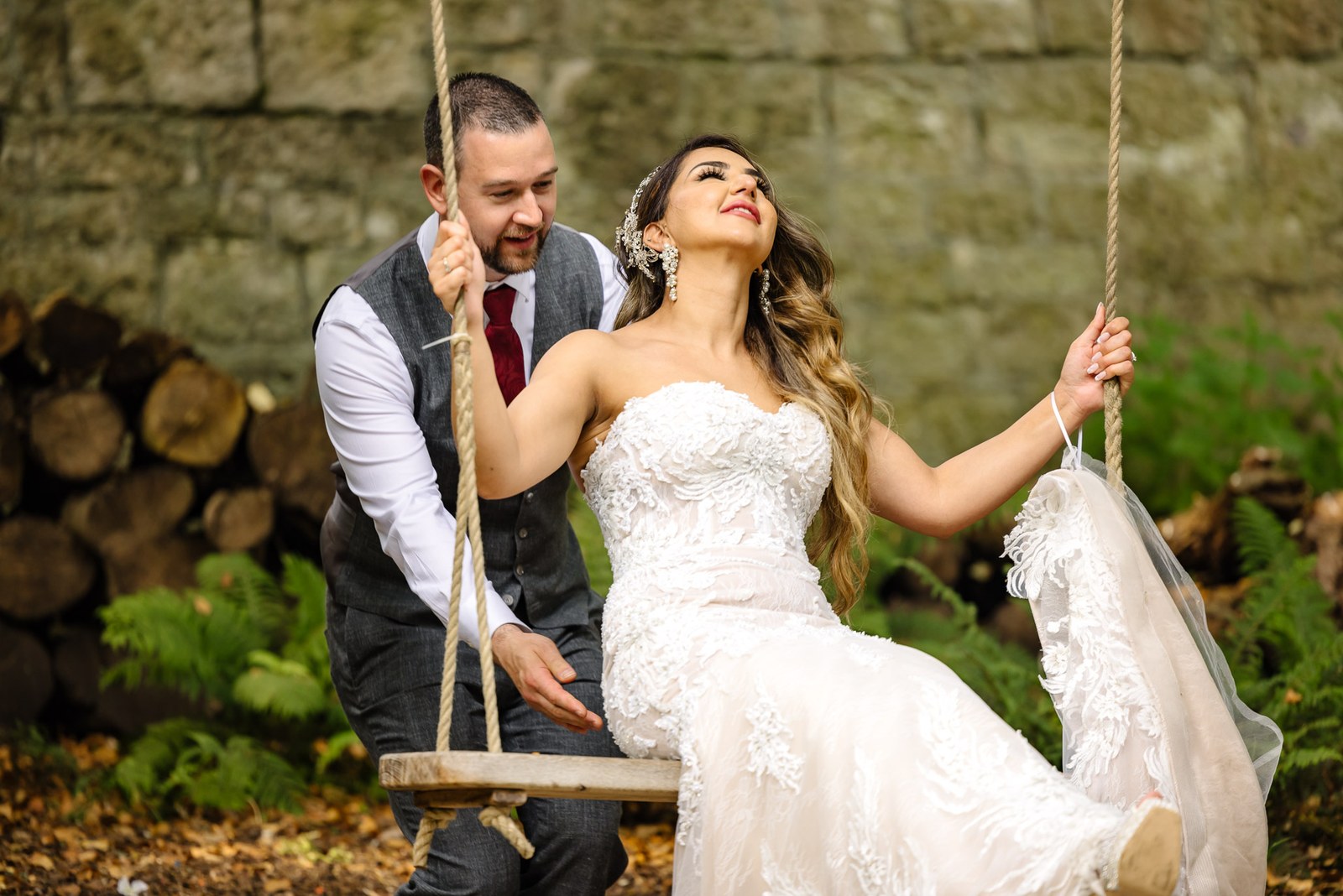 The groom laughing as he pushes the bride on a garden rope swing