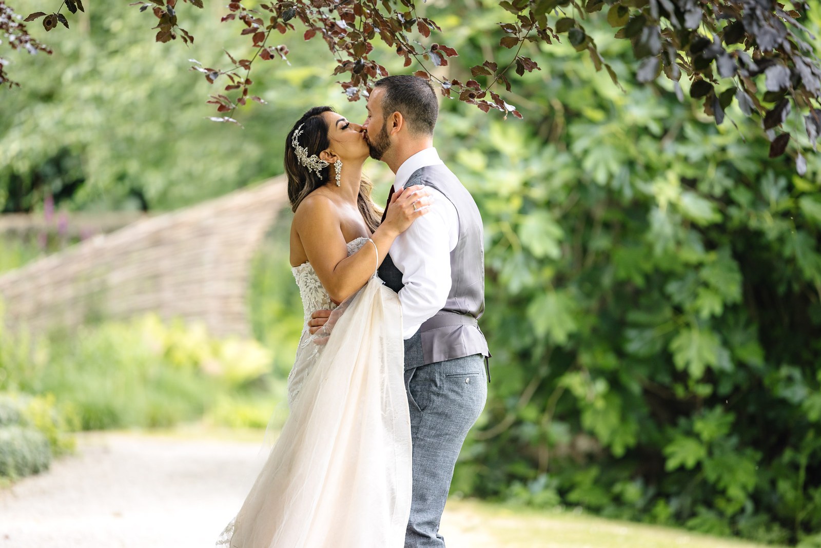 Bride and groom sharing a kiss beneath a tree in the grounds