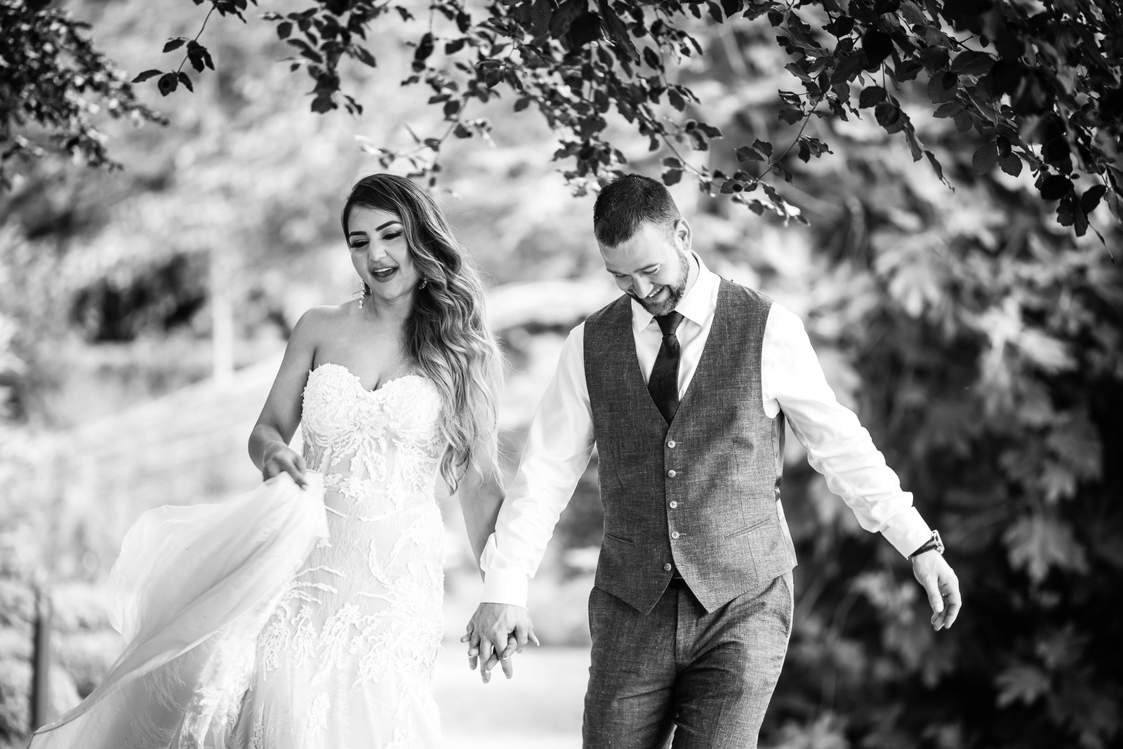 Black-and-white portrait of the couple walking hand in hand under a tree