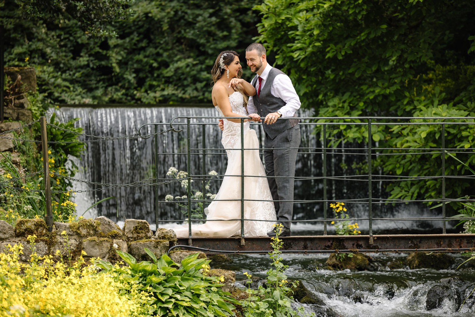 Bride and groom on a metal footbridge over the millstream in the gardens