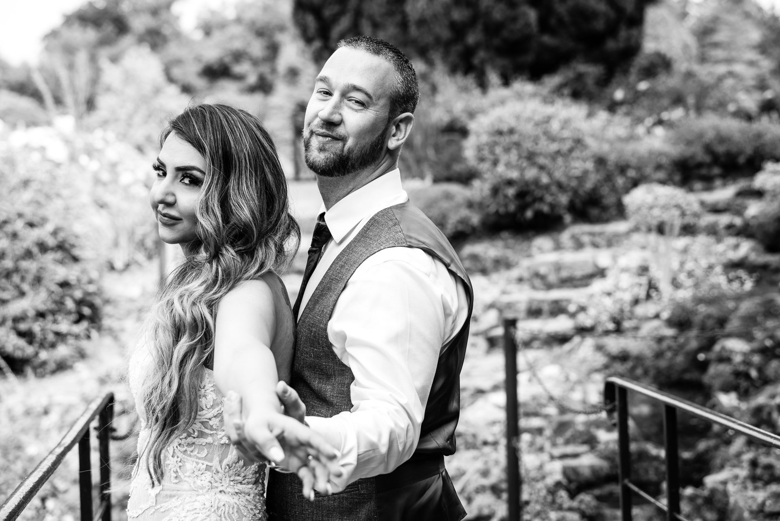 Black-and-white moment of the couple hand in hand on the garden footbridge
