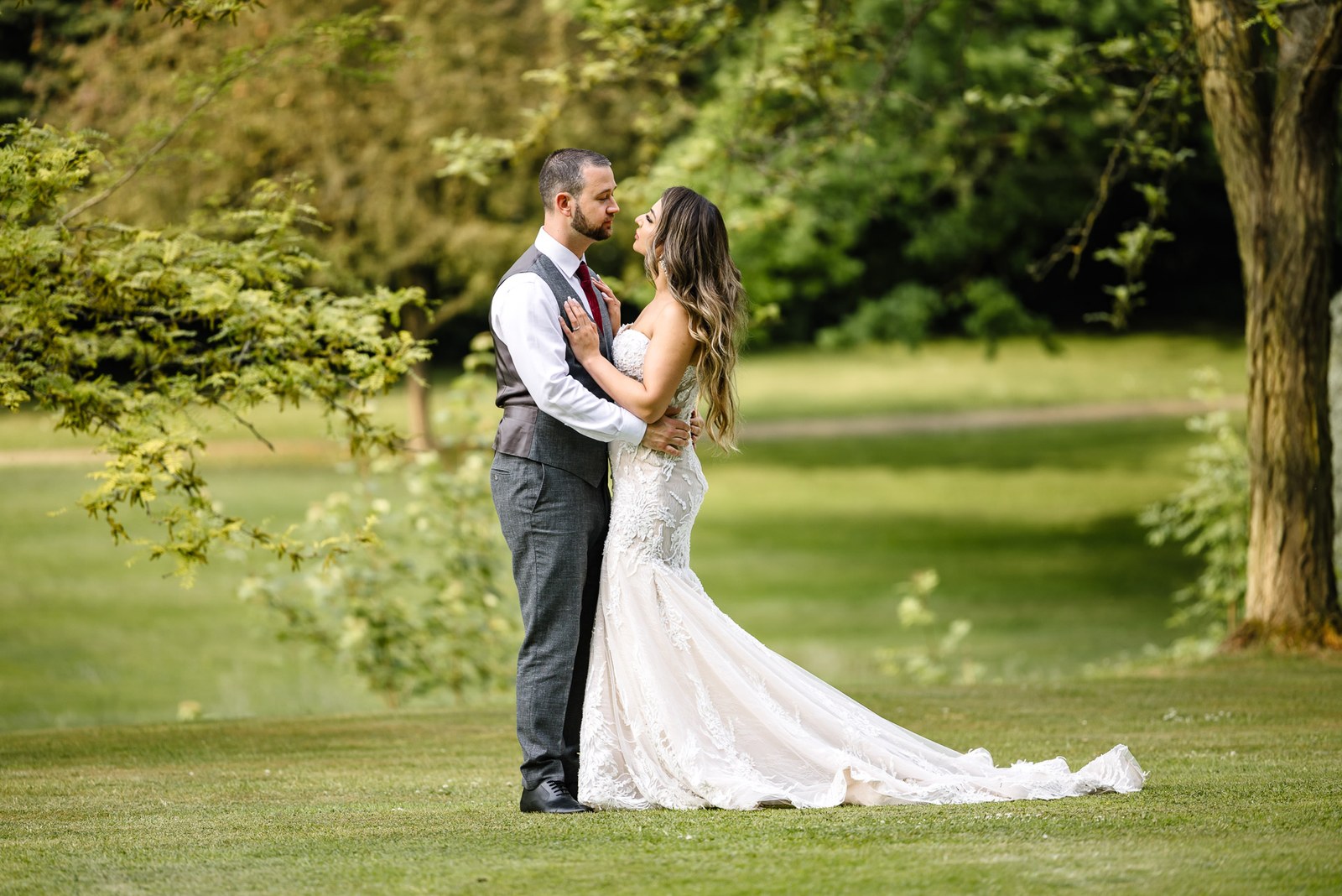 The couple embrace on the lawn beneath the trees