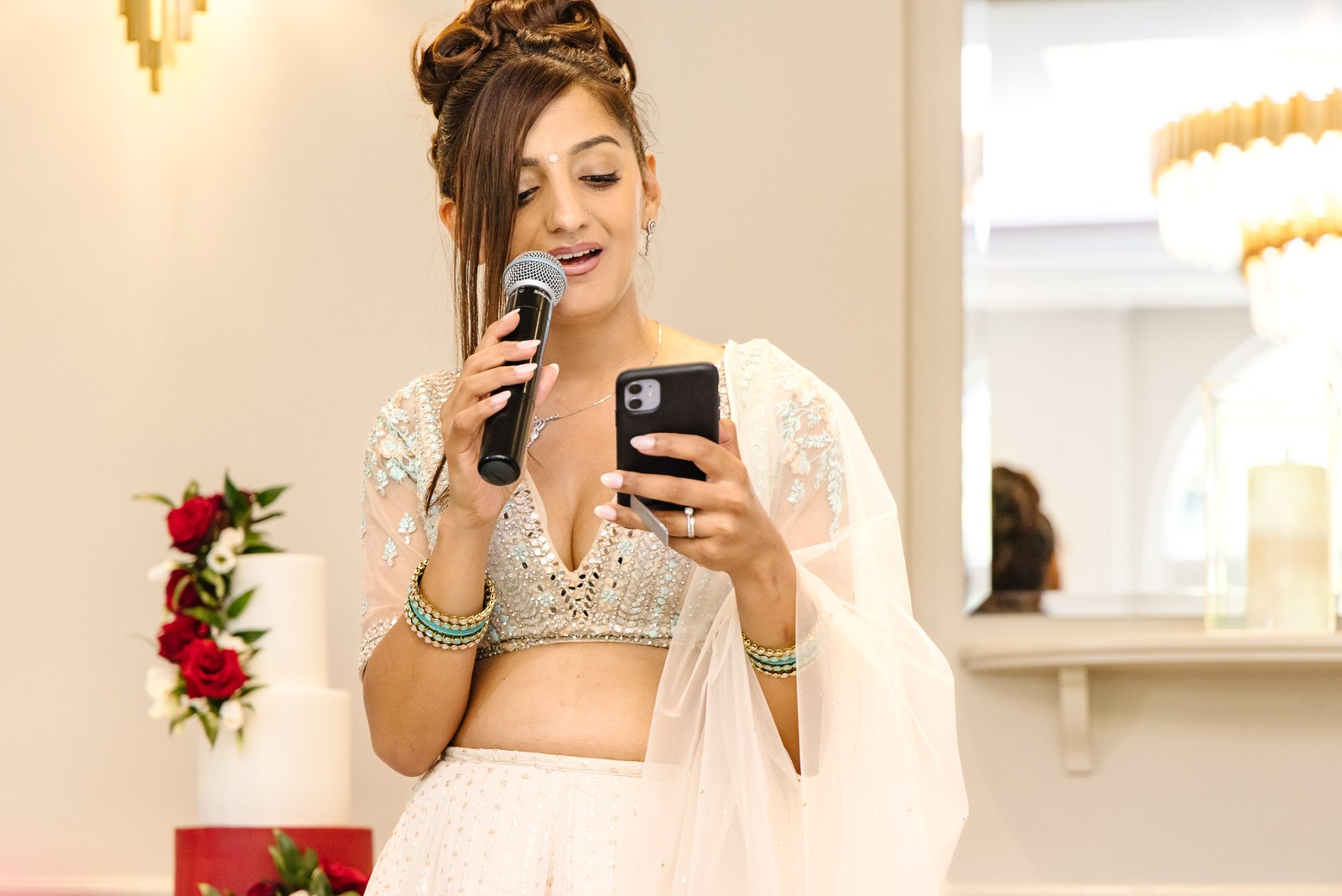 A guest gives a speech from her phone, the tiered cake behind her