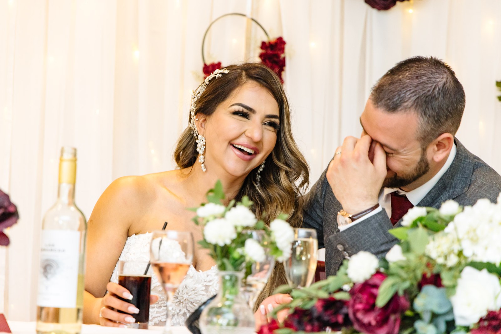 Bride laughing as the groom wipes a tear at the top table