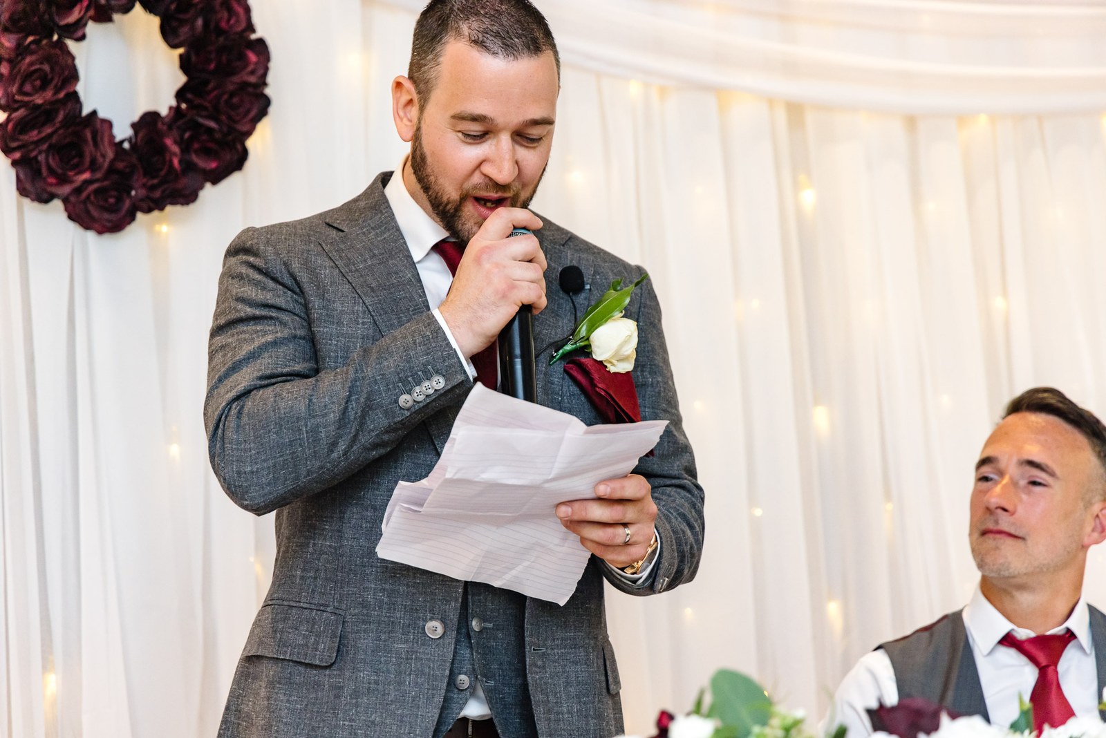 The groom delivers his speech from notes before a floral wreath backdrop