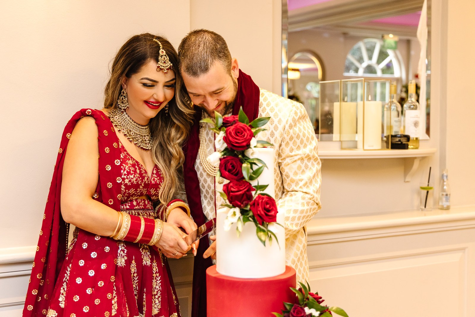 The couple in red and gold attire cut a red-and-white cake trimmed with roses
