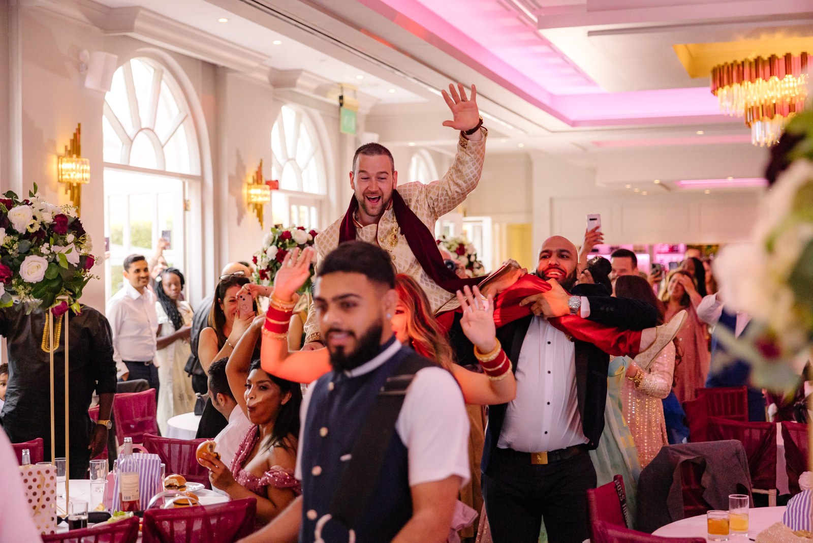 Guests cheer as the groom is lifted onto shoulders in the reception room